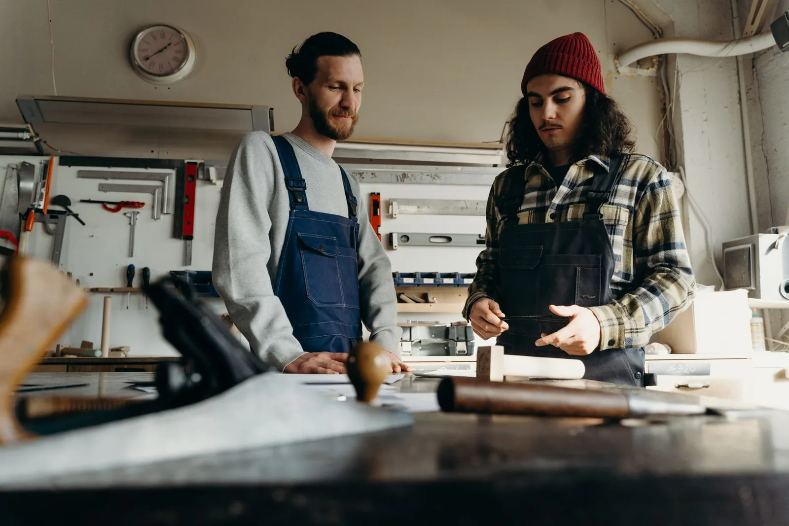 Two carpenters review a woodworking project together at a workshop bench.